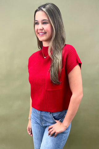 Woman wearing a red top and blue jeans against a green background