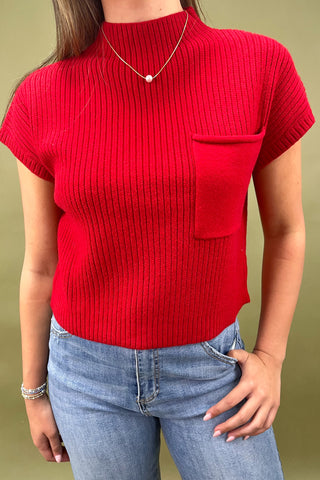 Person wearing a red ribbed top with a pocket and blue jeans on a beige background