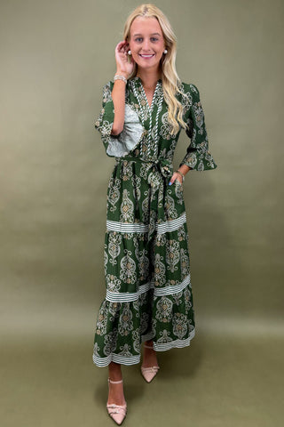 Woman wearing a purple top with white trim and blue jeans against a gray background