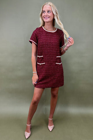 Woman wearing a maroon dress with white accents against a green background