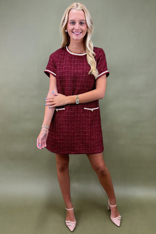 Woman wearing a maroon checkered dress with white accents against a green background
