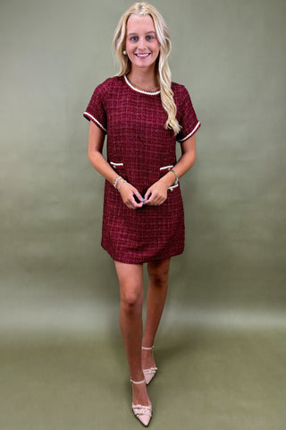 Woman wearing a maroon checkered dress against a plain background