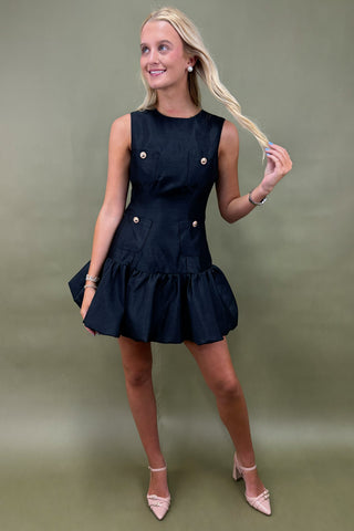 Woman wearing a black dress with white buttons against a green background