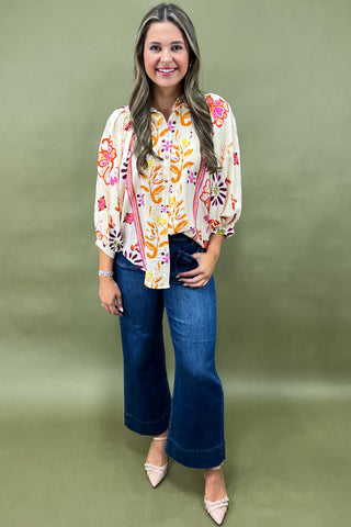 Woman wearing a floral blouse and blue jeans against a green background