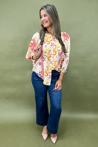 Woman wearing a colorful floral blouse and blue jeans against a green background