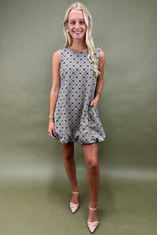 Woman wearing a gray sleeveless dress with black polka dots against a green background