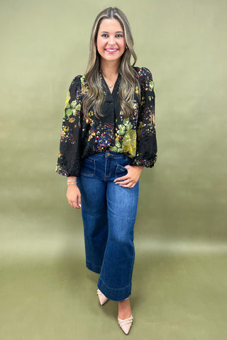 Woman wearing a floral blazer and blue jeans on a green background