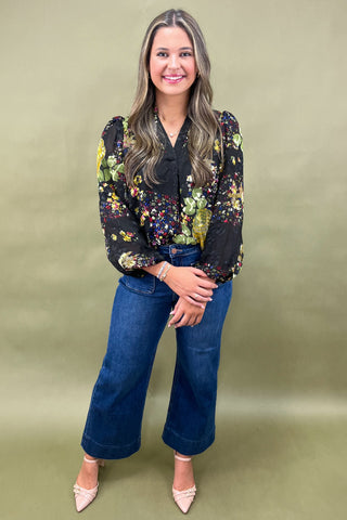 Woman wearing a floral blouse and blue jeans against a green background