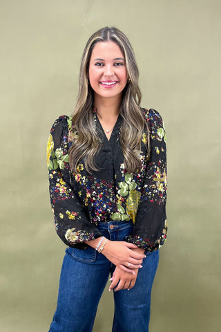Woman wearing a black floral blouse and blue jeans against a beige background