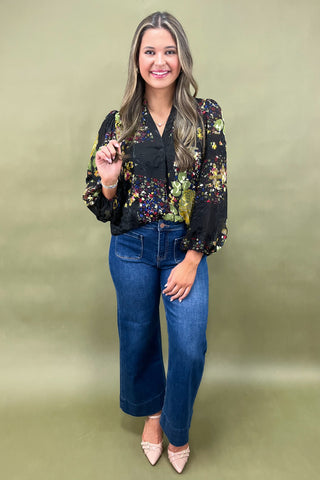 Woman wearing a floral blouse and blue jeans against a green background
