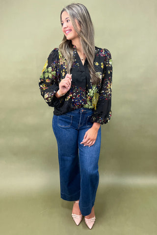 Woman wearing a floral blouse and blue jeans against a green background