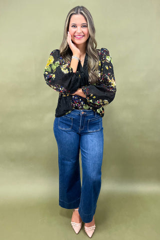 Woman wearing a floral blouse and blue jeans against a green background