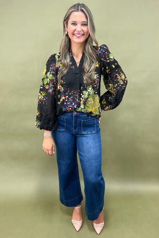 Woman wearing a floral blouse and blue jeans against a green background