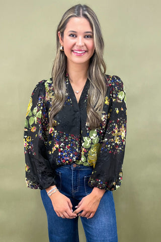 Woman wearing a black floral blouse and blue jeans against a beige background