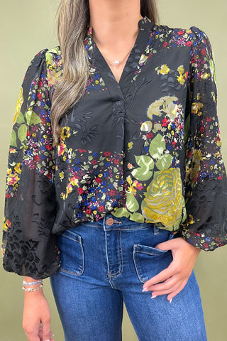 Person wearing a floral blouse with long sleeves and blue jeans against a green background
