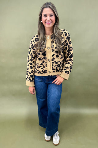 Woman wearing a leopard print cardigan and blue jeans against a green background
