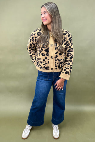 Woman wearing a leopard print cardigan and blue jeans against a green background