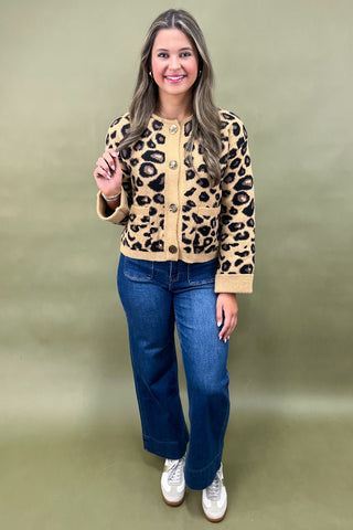 Woman wearing a leopard print cardigan, blue jeans, and white sneakers on a green background
