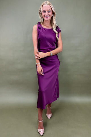 Woman wearing a purple dress with ruffled sleeves against a plain background