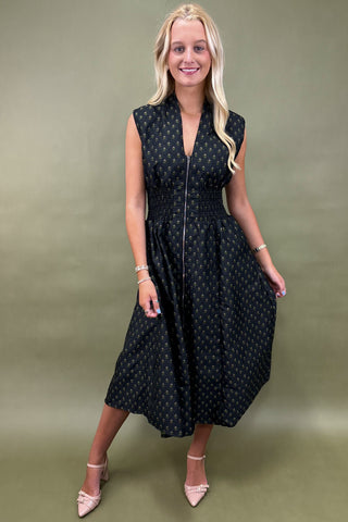 Woman wearing a black sleeveless dress with white patterns on a green background