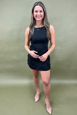 Woman wearing a black sleeveless top and floral skirt on a green background