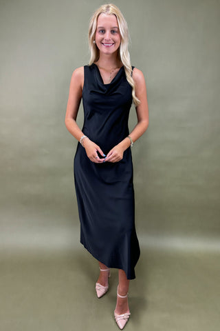 Woman wearing a black sleeveless dress against a plain background