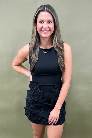 Woman wearing a black sleeveless top and floral black skirt against a green background
