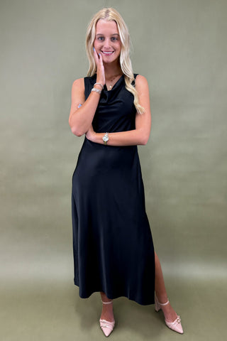 Woman wearing a black sleeveless dress with a slit on a green background