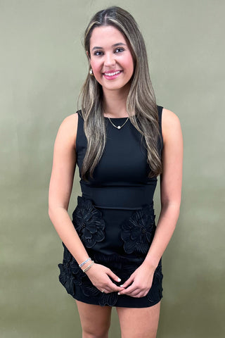 Woman wearing a black sleeveless top and black skirt against a green background