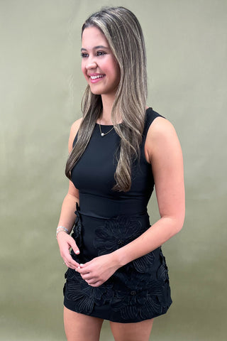 Woman wearing a black sleeveless top and black skirt against a plain background