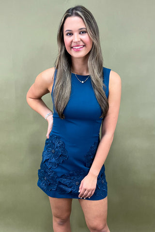 Woman wearing a blue dress with floral details against a green background