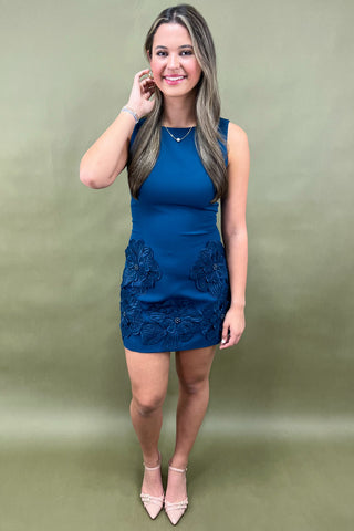 Woman wearing a blue dress with floral details on a green background
