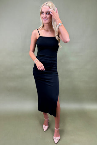 Woman wearing a black dress with a slit on a plain background