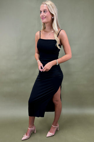 Woman wearing a black dress with a slit on a green background