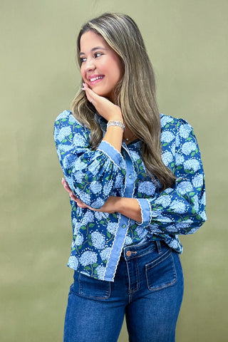Woman wearing a blue floral blouse and jeans against a green background