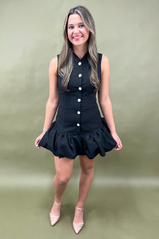 Woman wearing a black dress with white buttons against a green background