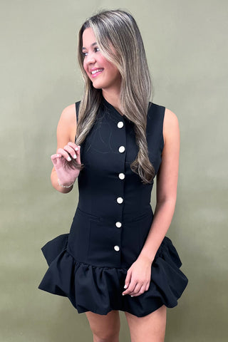 Woman wearing a black dress with white buttons against a plain background