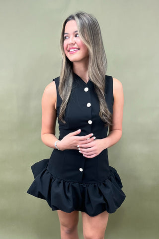 Woman wearing a black dress with white buttons against a green background