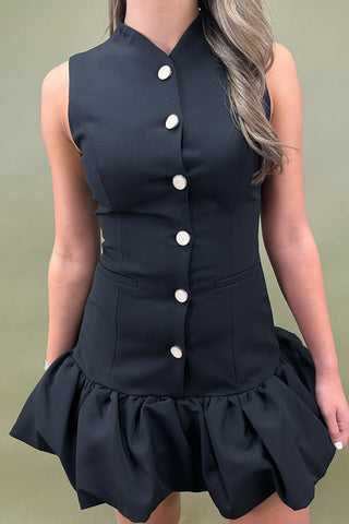 Black dress with white buttons on a plain background