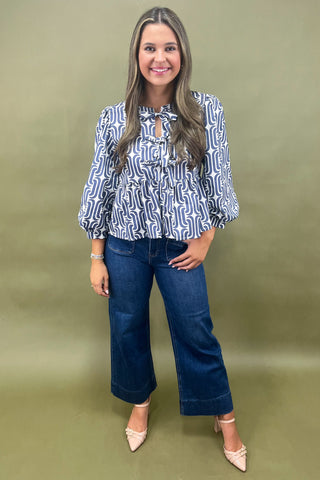 Woman wearing a patterned blouse and jeans against a green background