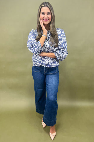 Woman wearing a patterned blouse and blue jeans against a green background