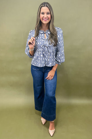 Woman wearing a patterned blouse and blue jeans against a green background