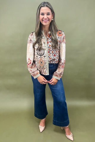 Woman wearing a patterned blouse and blue jeans against a green background