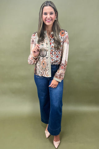 Woman wearing a patterned blouse and blue jeans against a green background