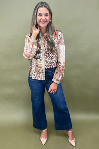 Woman wearing a patterned blouse and blue jeans against a green background