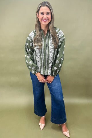 Woman wearing a green patterned blouse and blue jeans against a beige background