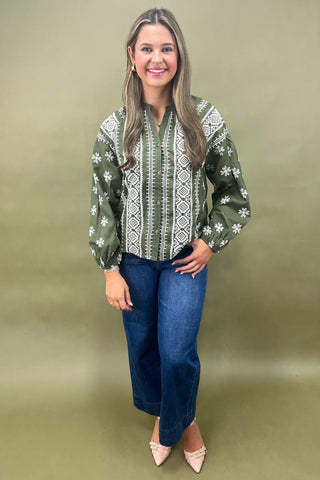 Woman wearing a green patterned blouse and blue jeans against a beige background