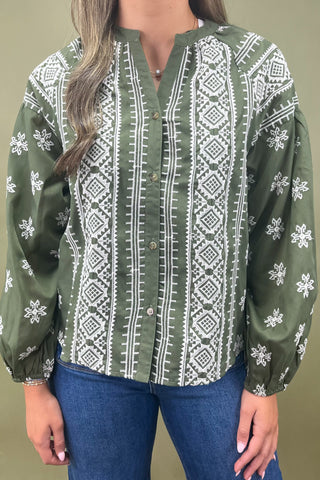 Green blouse with white patterns worn by a person on a beige background