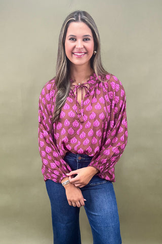 Woman wearing a pink patterned blouse and blue jeans against a beige background