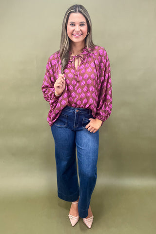Woman wearing a pink patterned blouse and blue jeans against a green background